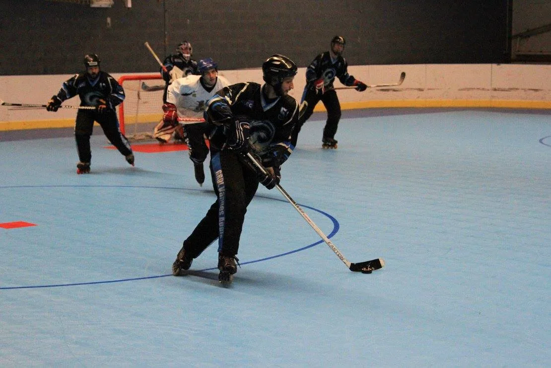 Des joueurs de roller hockey en patins en ligne disputent un match en salle.